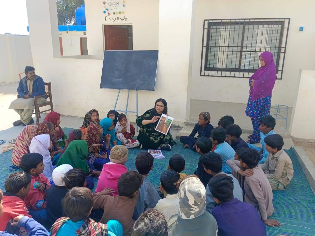 UNDP field officer teaching children - outdoor IRC classroom